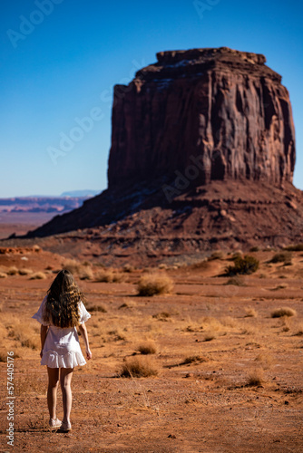 Beautiful long haired girl in white dress admires mighty unique famous rock formations in Monument Valley Navajo Tribal Park, Utah; Arizona, USA