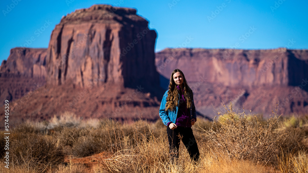 Naklejka premium girl in denim jacket walks through monument valley with massive monuments in the background; walk in the wild west, scene from a western