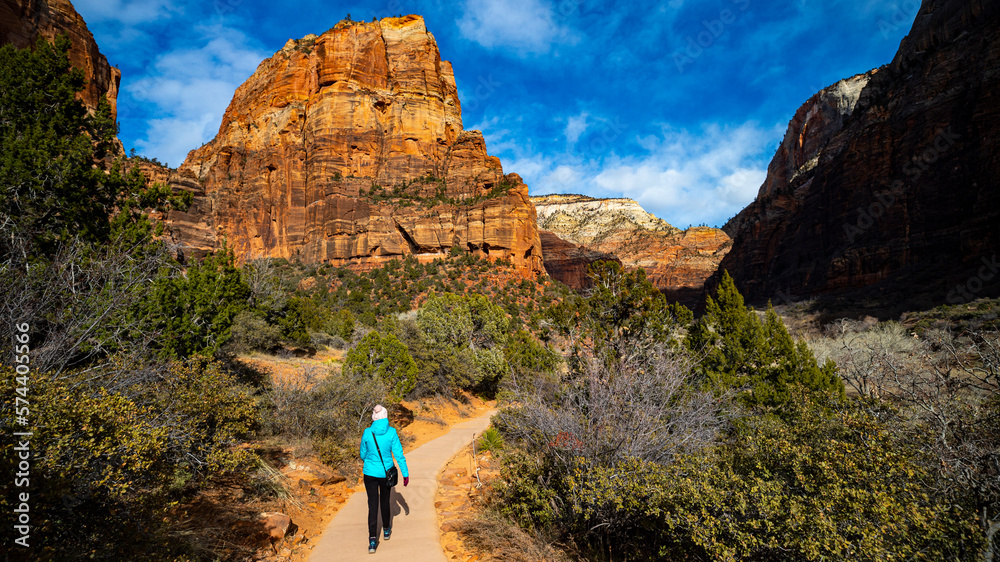A girl in a blue jacket hikes through the spectacular mountain scenery of Zion National Park in Utah, USA. Winter in Utah.