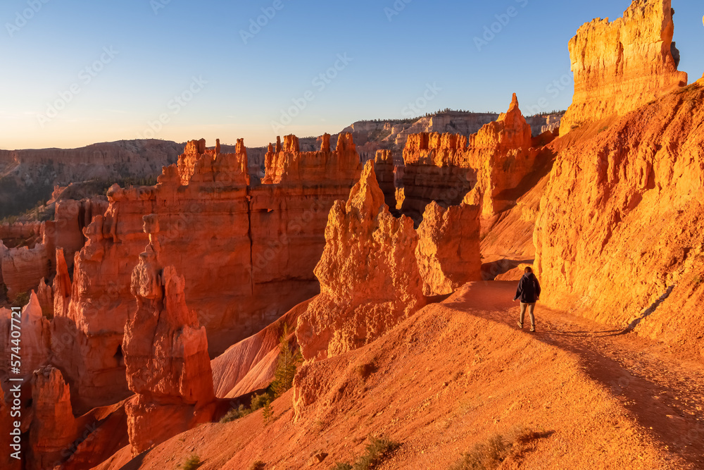 Woman hiking on the Navajo Rim trail next to Thor Hammer during sunset in Bryce Canyon National Park, Utah, USA. Scenic golden hour view of Sandstone Hoodoos in Bryce Canyon Amphitheatre on sunny day