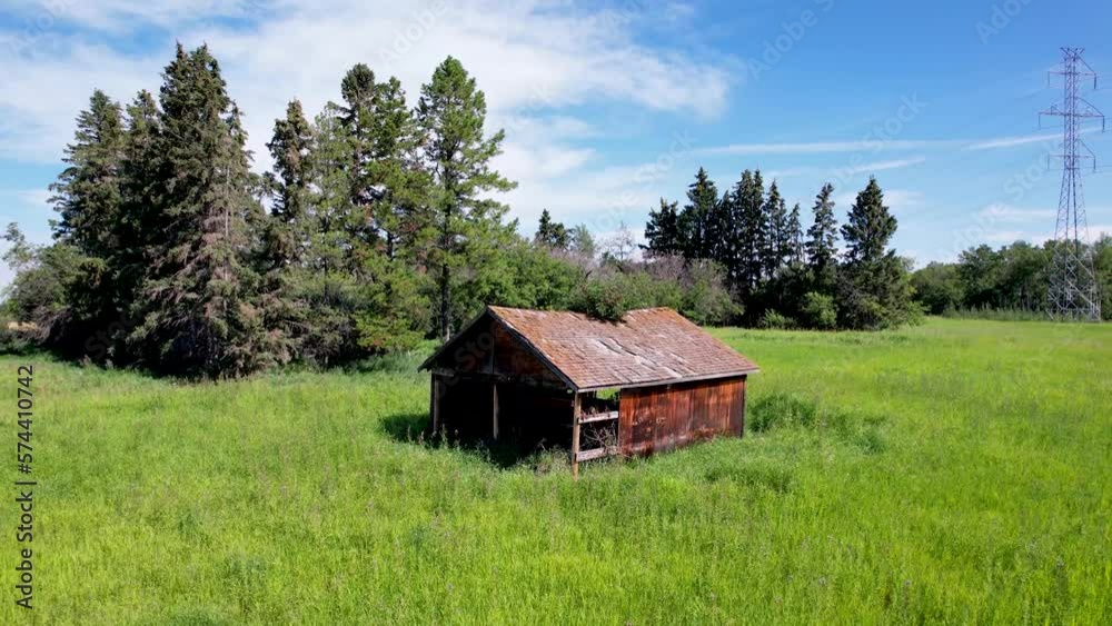 View of an old barn farming structure while the camera pulls back and flying upwards with a view of the barn surrounded by green grass, farmers field and high voltage powerlines in the background View of an old barn farming structure while the camera pulls back and flying upwards with a view of the barn surrounded by green grass, farmers field and high voltage powerlines in the background