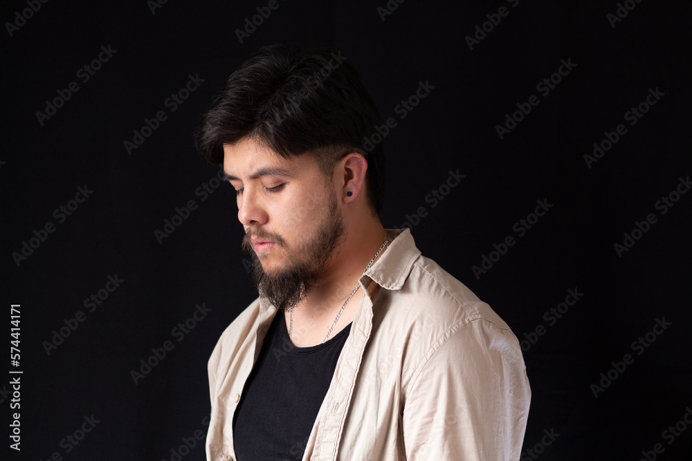 Medium close up shot of a young white man with a beard looking at the ground in front of a black background