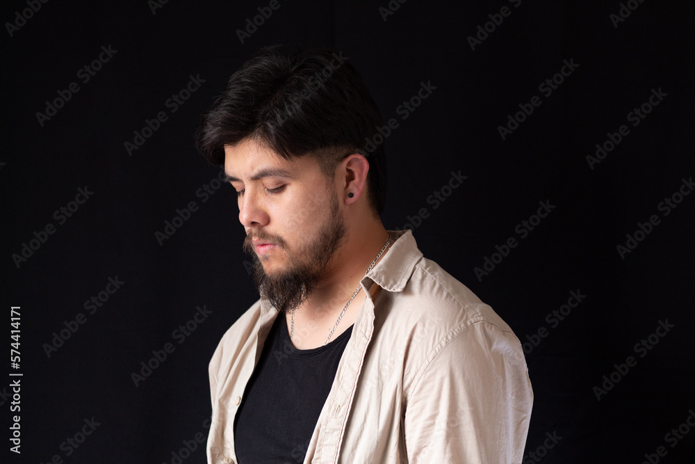 Medium close up shot of a young white man with a beard looking at the ground in front of a black background Medium close up shot of a young white man with a beard looking at the ground in front of a black background