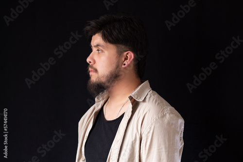 Medium close up shot of a young white man with a beard in profile in front of a black background