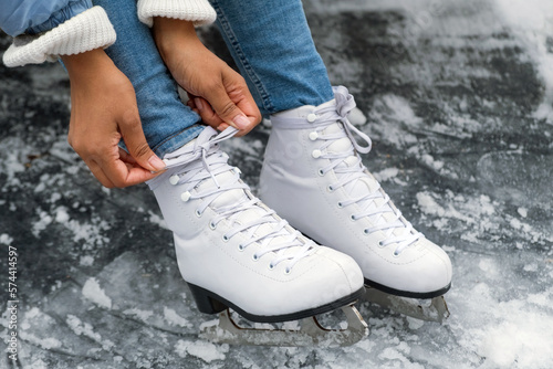 African American woman hands tying shoelaces on ice skates before skating on ice rink. Young African American woman prepares for skating