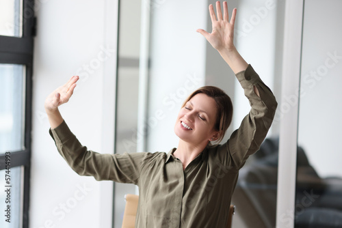 Happy woman at table in office raised her hands with joy
