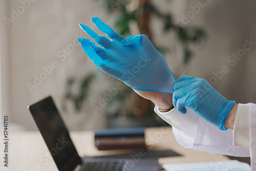 man doctor puts on medical gloves in office and works on laptop in clinic. male therapist prepares to receive patient, prescribes treatment with praparates. virologist, immunologist, endocrinologist