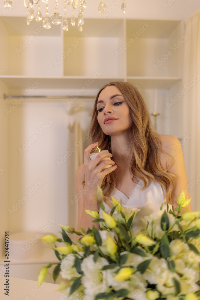 beautiful young fair-haired girl in a long white silk dress posing in a bright dressing room with beautiful flowers beautiful young fair-haired girl in a long white silk dress posing in a bright dressing room with beautiful flowers