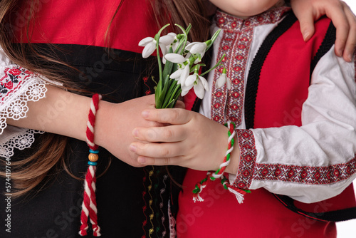 Bulgarian kids boy and girl in traditional folklore costumes with snowdrop flowers and handcraft wool bracelet martenitsa symbol of 1 March Baba Marta, spring and Easter, martisor photo