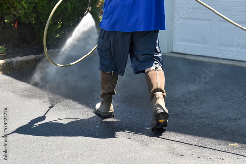Lower body of a handyman wearing shorts spraying water to pressure wash a driveway