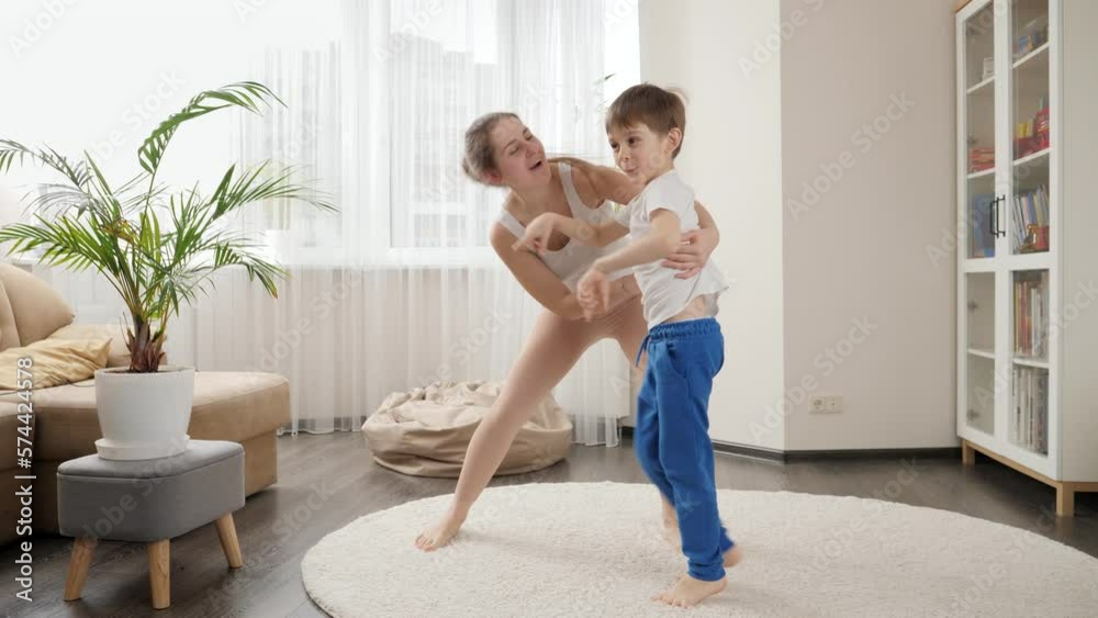 Funny shot of happy smiling mother playing and dancing with her little son in living room at home. Family having fun together, listening music, active lifestyle, parenting and child development. Funny shot of happy smiling mother playing and dancing with her little son in living room at home. Family having fun together, listening music, active lifestyle, parenting and child development.