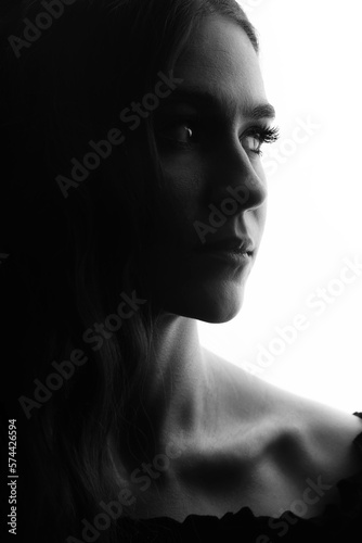 Close-up dark face silhouette of beautiful and sexy woman with dark wavy hair. Part of model face illuminated with light. Sensual mood. Lips in camera focus. Black and white image
