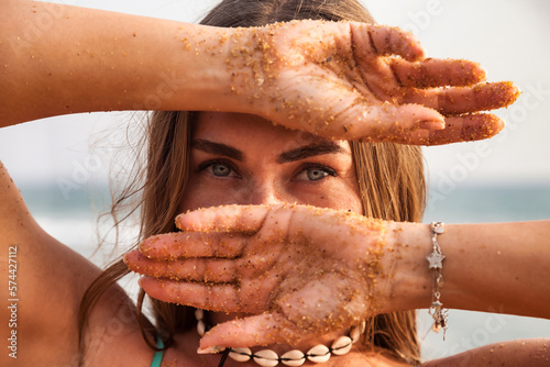 Close up of eyes pretty young lady model with hands near face at tropic ocean background, looking at camera. Face cute woman posing with hands. Beauty fashion industry concept. Copy advertising space
