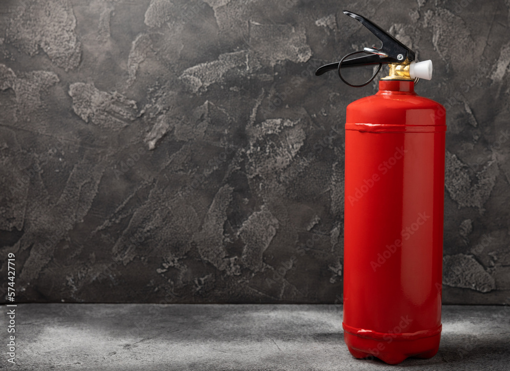 Fototapeta premium Fire extinguisher on the background of a black texture wall. Red fire extinguisher indoors on the wall. Fire protection, home fire extinguisher. Mockup, space for text, copy space.