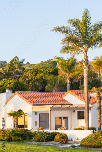 Beautiful houses with nicely landscaped front the yard, and green hills in the background in a small beach town in California at sunset