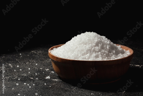Coarse white salt in a wooden bowl on the black background