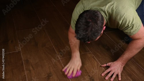 middle aged Caucasian man on hands and knees scrubbing the floor by hand with a cloth. The person is thoroughly cleaning the house as an unenjoyable yet mandatory chore in daily life