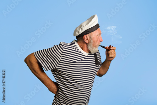 Cheerful sailor on a blue background in profile. Copy space. Old sailor with a smoking pipe