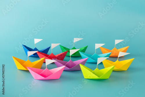 Colorful paper ships on blue background with white flags indicate direction, unity, competition, goals, team group concept.