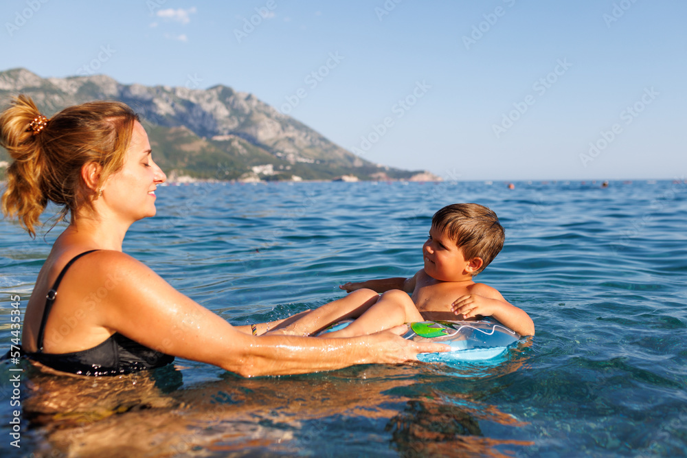 Caring mother rides her son on an inflatable ring in the sea Caring mother rides her son on an inflatable ring in the sea