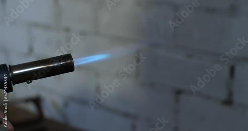 A man's hand holds and turns on a blowtorch. The blowtorch flashes brightly after being turned on and burns with a steady blue flame. photo