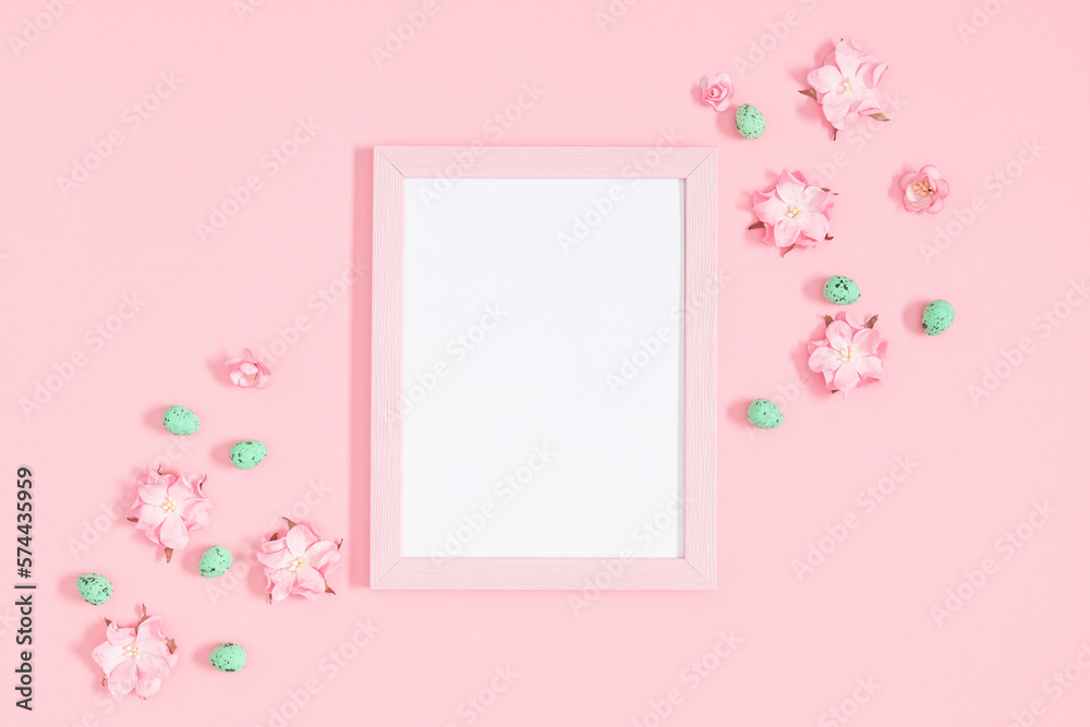 Easter decor, composition. Empty photo frame, flowers, easter eggs on pastel pink background. Flat lay, top view, copy space
