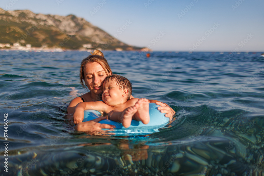 Fototapeta premium Caring mother rides her son on an inflatable ring in the sea