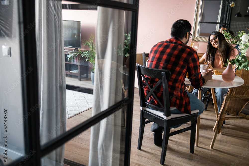 Happy couple eating breakfast and talking at dining table in morning. Indian girl and latino guy. Relationship and diversity concept