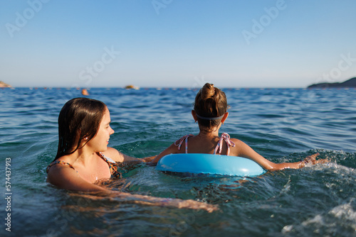 Fotografia Two sisters in bathing suits play with an inflatable ring in the sea