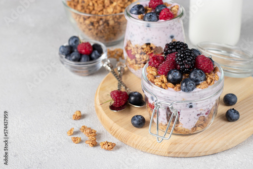 Chocolate granola with berries, chia seeds and natural yogurt in two jars on wooden board on gray background