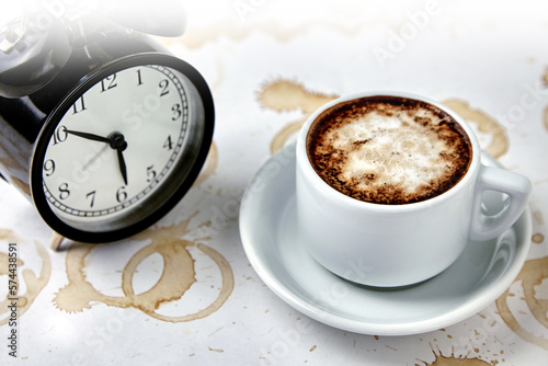 A cup of coffee, cappuccino and a clock with a white table with coffee stains