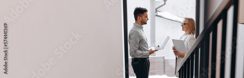 Two business people man and woman are standing opposite each other in a large corridor and talking. Concept of successful business.