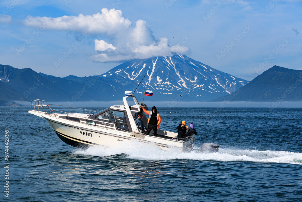 Fototapeta premium A boat with tourists floats in the Pacific Ocean against the backdrop of a snow-covered volcano and mountains.