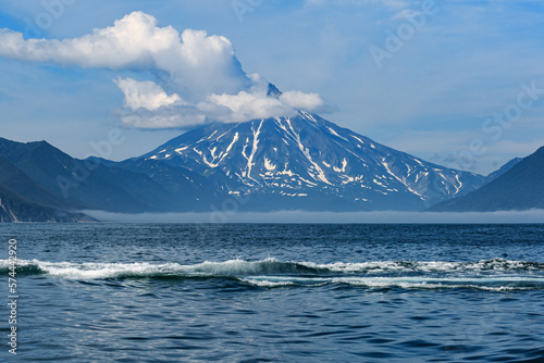 Rocks and mountains of various shapes, in the Pacific Ocean, against the backdrop of a volcano, a clear sunny day, clouds, Kamchatka.