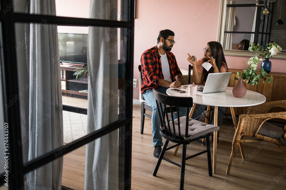 Young millennial indian husband and wife doing domestic paperwork, accounting job and reviewing paper bills, receipts at laptop computer, using online calculator and paying mortgage rent fees on Young millennial indian husband and wife doing domestic paperwork, accounting job and reviewing paper bills, receipts at laptop computer, using online calculator and paying mortgage rent fees on