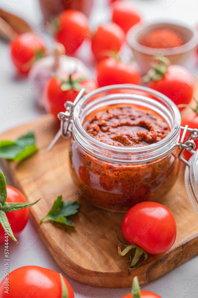 Salsa or adjika sauce is a traditional Mexican or Caucasus sauce with tomatoes and hot peppers on a light background with fresh herbs close up. Concept of a vegetarian food. Salsa or adjika sauce is a traditional Mexican or Caucasus sauce with tomatoes and hot peppers on a light background with fresh herbs close up. Concept of a vegetarian food.