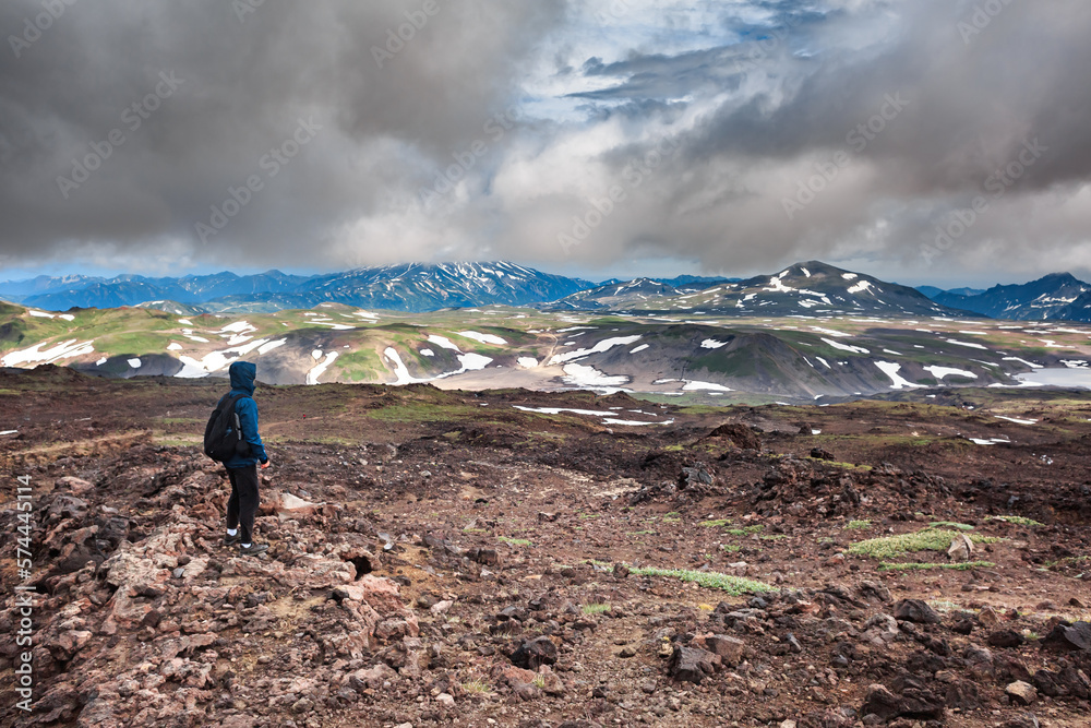 A tourist stands against the backdrop of a volcano, trekking, Kamchatka, tourists, mountains, clouds.