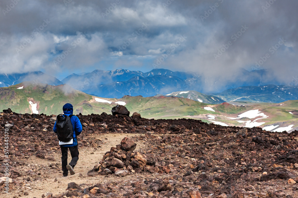 A tourist walks on volcanic sand, against the backdrop of a volcano, trekking, Kamchatka, tourist, mountains, clouds.