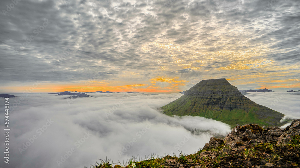 Panorama von Bergspitzen die aus den Wolken auf den Färör Inseln beim Sonnenuntergang ragen und schaffen eine mystische Stimmung.