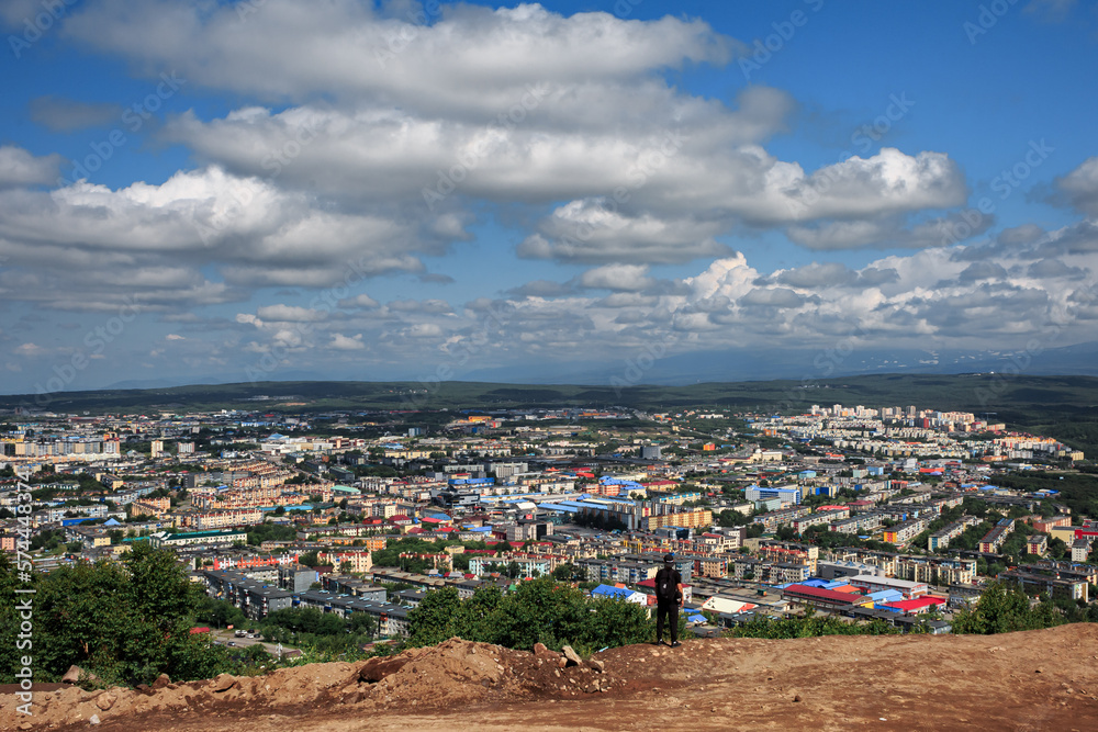 A man stands on a mountain cliff, against the backdrop of Petropavlovsk-Kamchatsky, on a clear sunny day, clouds, a volcano.