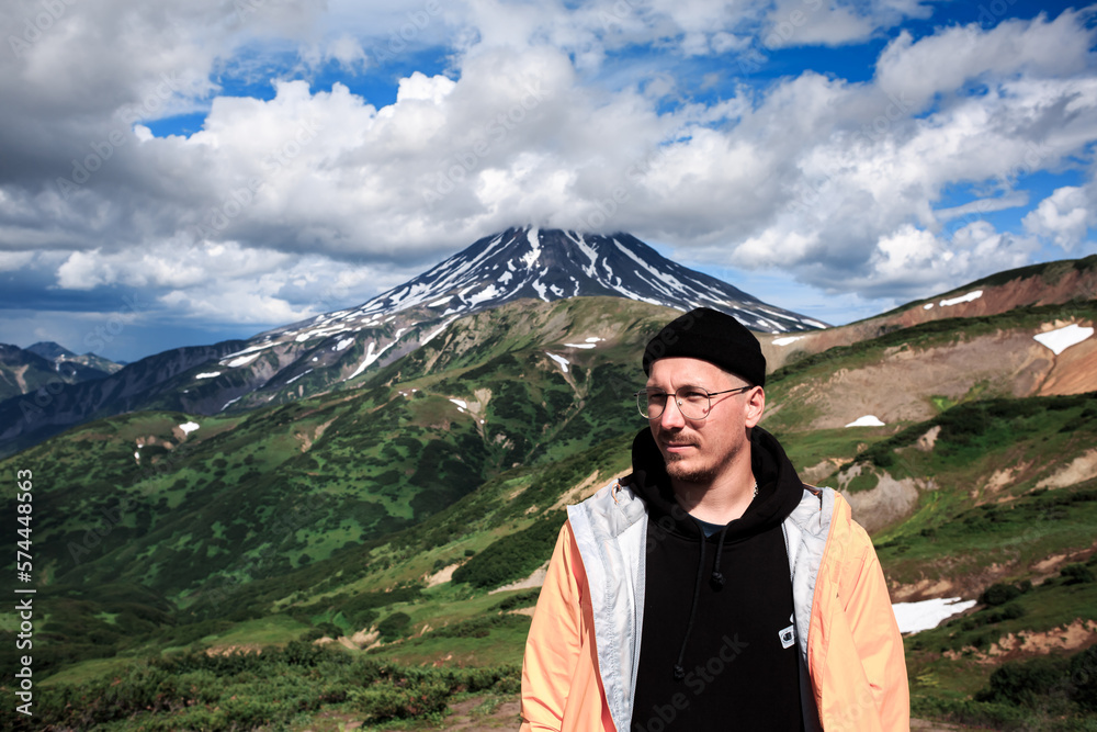 Portrait of a man in glasses against the backdrop of a volcano and green meadows, mountains.