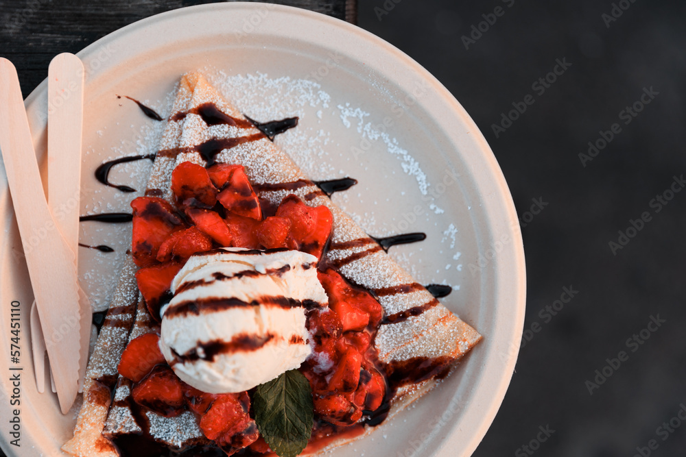 One scoop of vanilla ice cream on top of strawberries on top of crepe with chocolate and powdered sugar