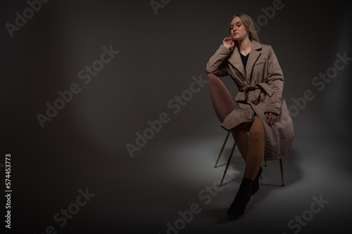 portrait of a young, emotional girl sitting on a chair in a flirtatious mood, gesturing with her hands, empty space, wearing a jacket, a dark cloak on an isolated white background, space for text