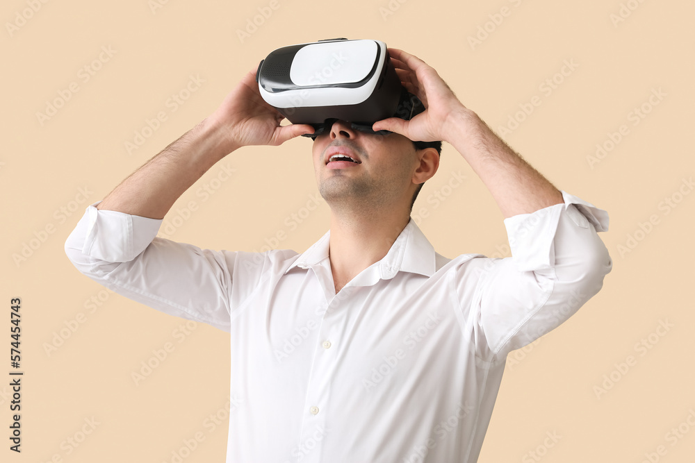 Young man using VR glasses on beige background