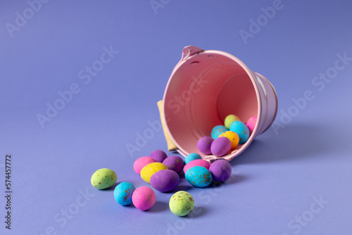 Image of multi coloured easter eggs and bucket with copy space on purple background