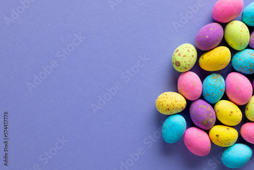 Image of multi coloured chocolate easter eggs with copy space on purple background