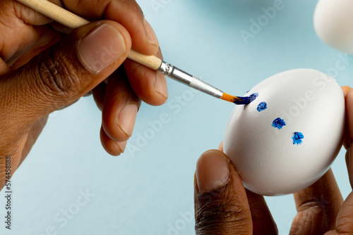 Image of hands of african american woman painting easter eggs with copy space on blue background
