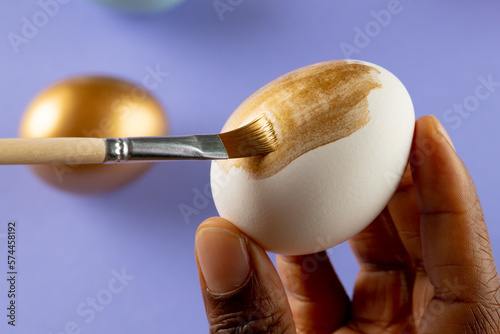 Image of hands of african american woman painting easter eggs with copy space on purple background