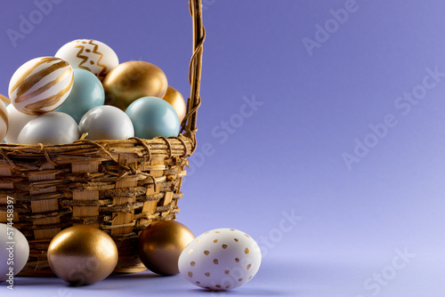 Image of multi coloured easter eggs in basket and copy space on purple background