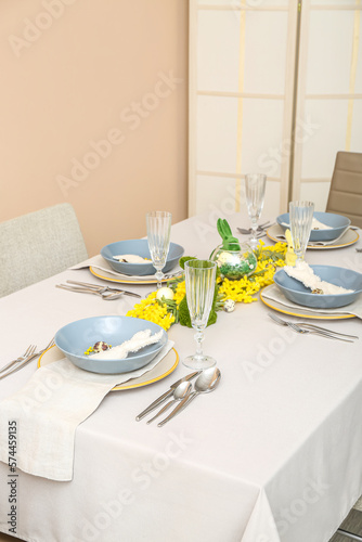 Festive table setting with eggs, bunnies and mimosa flowers served for Easter celebration